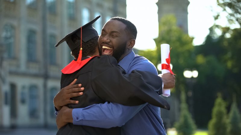 Cheerful father and graduating son hugging outdoor, study achievement, education